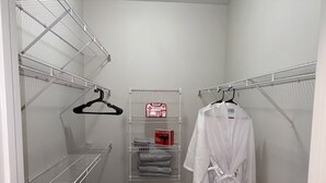 A walk-in closet with metal shelves, a hanging robe, and a Revlon box. - Chic Apt in The Woodlands-Parking-WI-FI-King Bed (Conroe)
