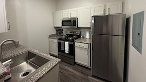 A modern kitchen with stainless steel appliances, white cabinets, and a granite countertop. - Chic Apt in The Woodlands-Parking-WI-FI-King Bed (Conroe)