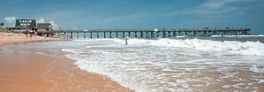 En strandscen med en pir som sträcker sig ut i havet, en skylt med texten ”FLAGLER BEACH” och ett livräddartorn.