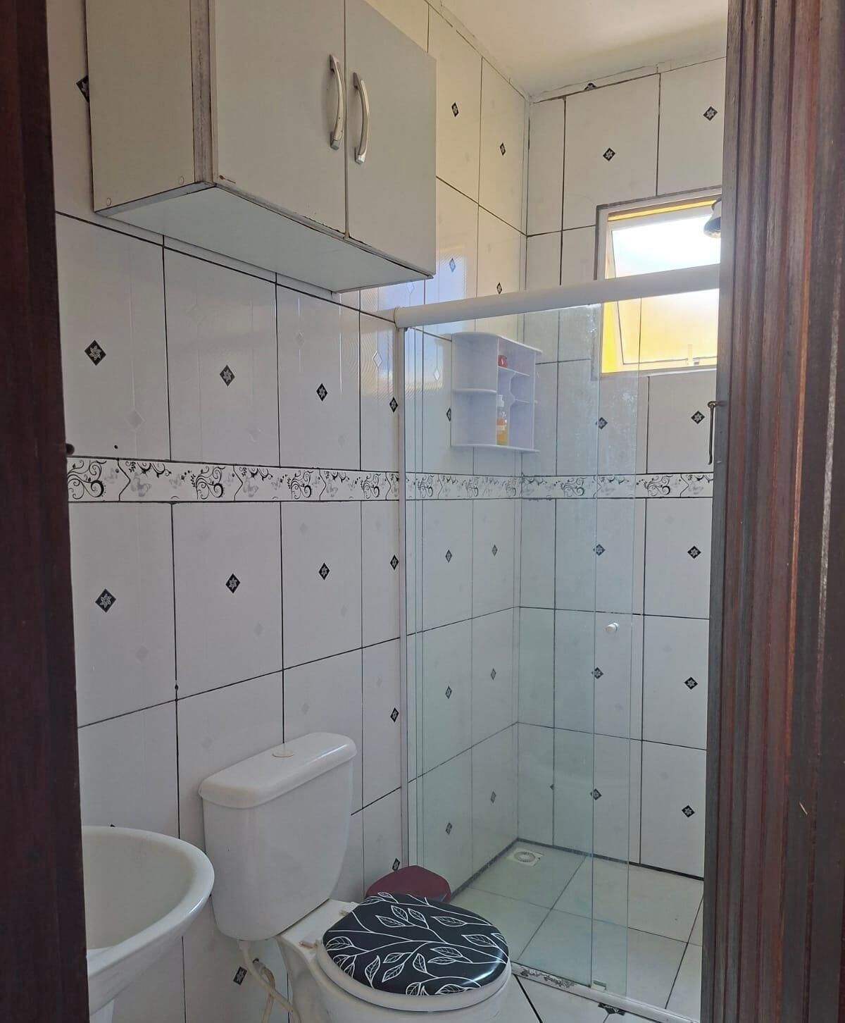 A small bathroom with white tiles, a toilet, a sink, and a shower area.
