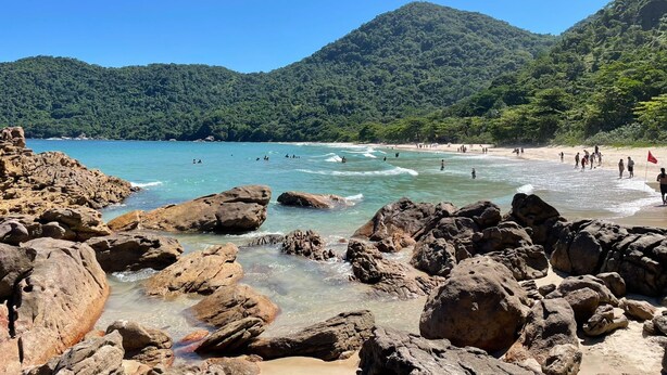 A rocky beach with clear water and a forested hill in the background. - Tabalipa House. (Paraty)