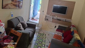 A living room with a sofa, a couch, a flat-screen TV mounted on a wooden wall, a patterned rug, and a painting of a beach scene. - Tabalipa House. (Paraty)