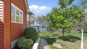 A house with a red exterior, a window, a porch, a lawn, and a tree. - Stunning Lakefront Retreat set on a Private point on North Pond, 9 acres w/beach (Smithfield)