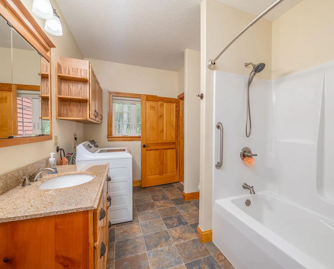 Une salle de bain équipée d’un lavabo, d’un miroir, de meubles en bois, d’une machine à laver et d’une baignoire.