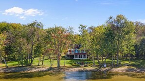 A lakeside property with a large house surrounded by trees and a grassy area. - Stunning Lakefront Retreat set on a Private point on North Pond, 9 acres w/beach (Smithfield)