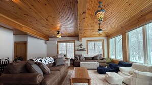 A cozy living room with wooden ceilings, large windows, and a fireplace. - Stunning Lakefront Retreat set on a Private point on North Pond, 9 acres w/beach (Smithfield)