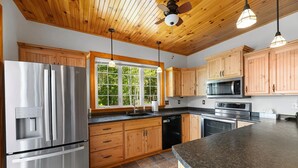 A modern kitchen with wooden cabinets, stainless steel appliances, and a large window providing natural light. - Stunning Lakefront Retreat set on a Private point on North Pond, 9 acres w/beach (Smithfield)