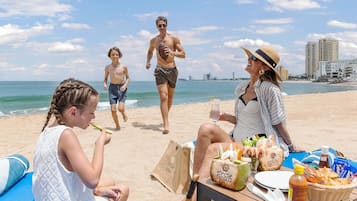 A beach scene with people, a table with food and drinks, and a city skyline in the background.