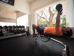 A gym with exercise equipment, a water dispenser, and a large window with a tree view.