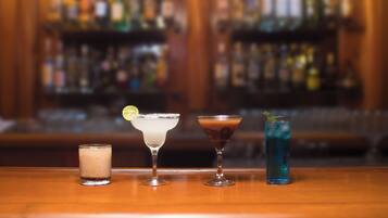 Tres bebidas sobre una barra, con un fondo borroso de estantes llenos de botellas.