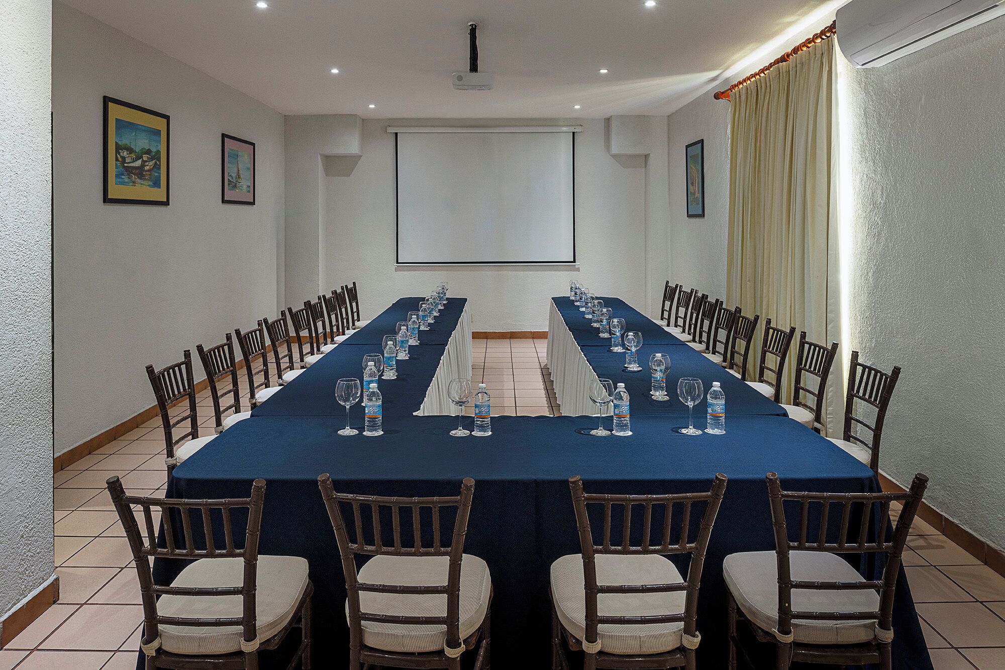 Un salón de conferencias con una mesa larga, sillas, botellas de agua y vasos.