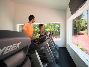 Une salle de sport équipée de tapis de course, d’un téléviseur et offrant une vue sur la verdure environnante.