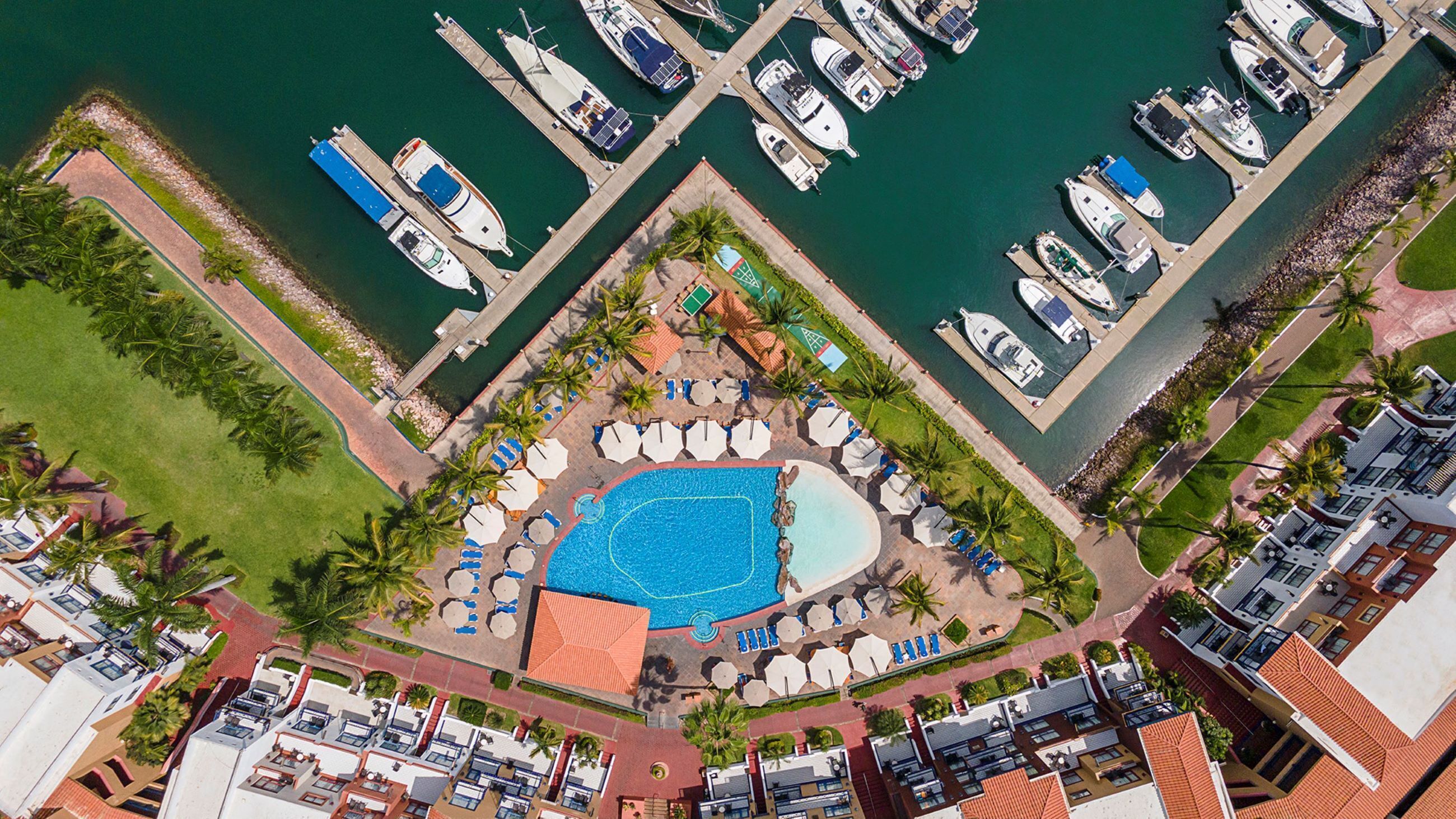 Vista aérea de uma marina com barcos atracados, uma piscina e edifícios em estilo resort.