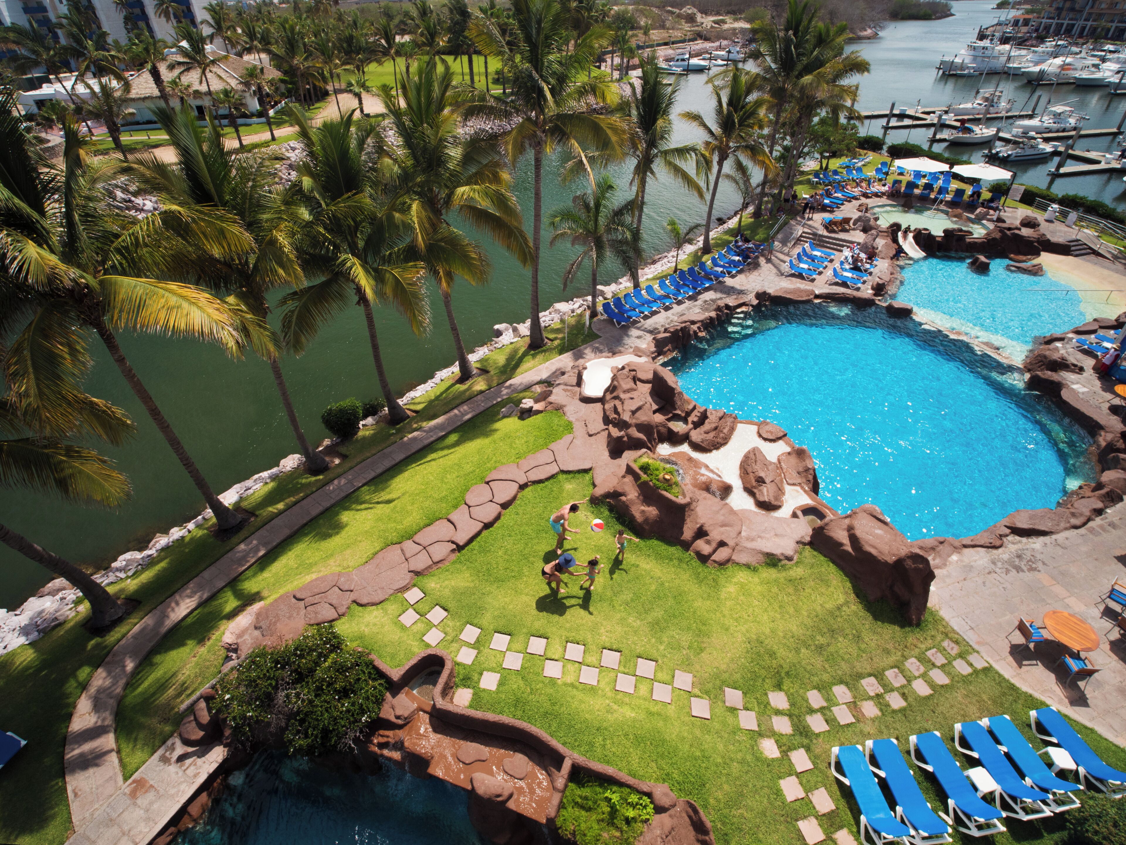 A resort with a large pool, palm trees, and a marina.