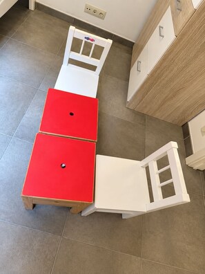Una habitación con un armario blanco, una mesa roja y una silla blanca.