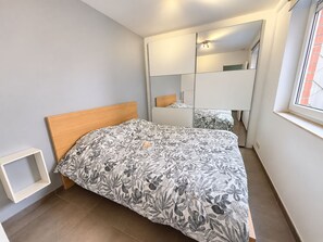 Ein Schlafzimmer mit Bett, Schrank, Spiegel und Fenster.