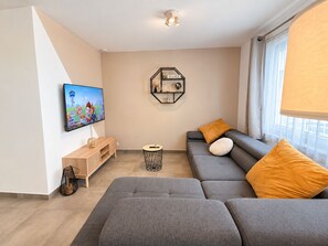 A modern living room with a flat-screen TV, a sofa, a coffee table, and a decorative shelf. - Familytime (Oostende)