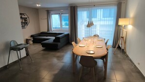 A modern living room with a dining table, sofa, and a lamp. - Familytime (Oostende)