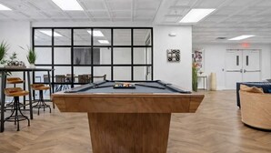 A billiards table in a room with a modern design, featuring a large window, a bar area, and a seating space with a sofa. - Lux 3BR w 3 King Beds, Downtown, Parking (Charlotte)