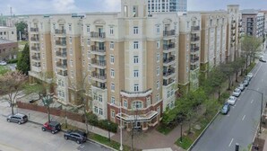 A multi-story residential building with balconies, a parking area, and a street view. - Lux 3BR w 3 King Beds, Downtown, Parking (Charlotte)