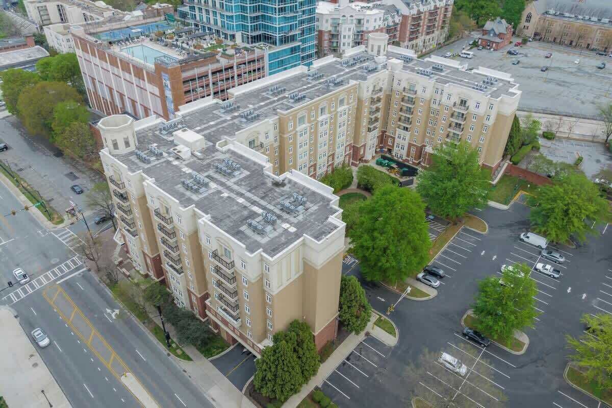 Vista aérea de un edificio de varios pisos con estacionamiento y zonas verdes circundantes.