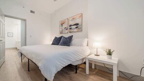 Ein modernes Schlafzimmer mit einem großen Bett, einem Nachttisch mit Lampe und zwei abstrakten Bildern an der Wand.