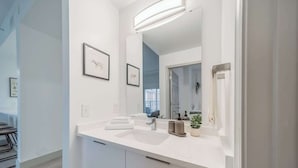 A modern bathroom with a white countertop, a large mirror, and framed artwork on the wall. - Uptown 4 Bed w Balcony Downtown, Parking (Charlotte)