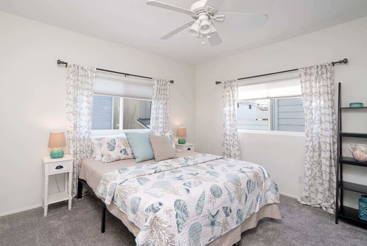 A bedroom with a bed, two nightstands, a ceiling fan, and a window with curtains.