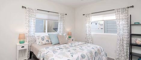 A bedroom with a bed, two nightstands, a ceiling fan, and a window with curtains.