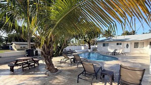 Un espace aménagé au bord de la piscine, avec des chaises longues, une table de pique-nique et un palmier.