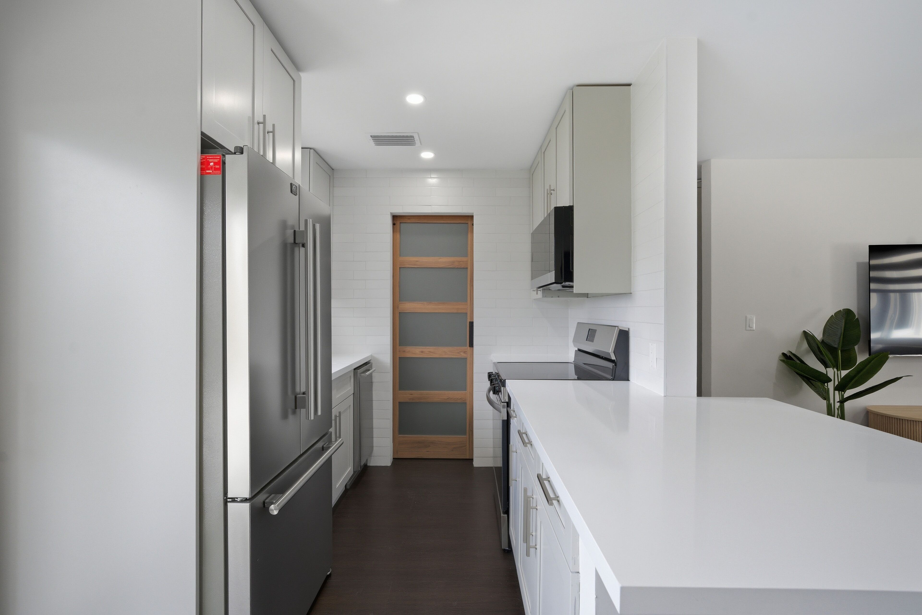 A modern kitchen with white cabinetry, a stainless steel refrigerator, and a wooden door.