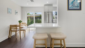 Une cuisine moderne avec un plan de travail blanc, des appareils en acier inoxydable et des chaises en bois.