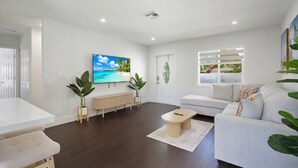 Un salon moderne avec un canapé blanc, une table basse et un téléviseur diffusant une scène de plage.