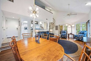 Un vaste espace de vie comprenant une table à manger en bois, des fauteuils à motifs bleus et un lustre moderne.