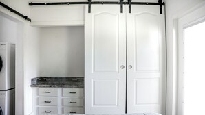 Quarto com cama, guarda-roupa com porta deslizante, máquina de lavar embutida e bancada.