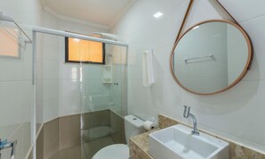 A modern bathroom with a glass shower enclosure, a round mirror, a sink with a marble countertop, and a toilet. - Casa em Cond. c/ piscina em Camaçari BSP0008 (Camaçari)