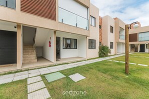 A modern building with a flat roof, large windows, and a paved walkway. - Casa em Cond. c/ piscina em Camaçari BSP0008 (Camaçari)