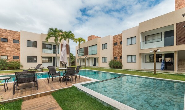 A modern hotel with a swimming pool, outdoor seating, and a well-maintained garden. - Casa em Cond. c/ piscina em Camaçari BSP0008 (Camaçari)