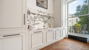 Une cuisine avec des meubles blancs, un pare-feu en marbre et une vue sur l’extérieur.