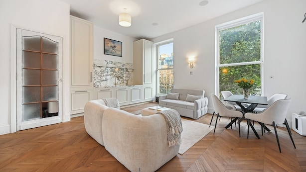 Un salon moderne comprenant un canapé, une table à manger avec des chaises, et offrant une vue sur l’extérieur grâce à de grandes fenêtres.