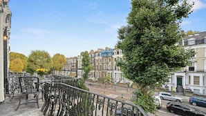 Un balcon orné de balustrades en métal noir, une rangée de maisons mitoyennes et un arbre aux fleurs jaunes.