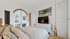 Une chambre à coucher avec un lit, une commode, un téléviseur et un tableau accroché au mur.