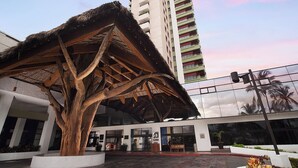 A modern building with a large tree sculpture in front, a glass facade, and a red brick pathway. - El Cid El Moro Beach Hotel - All Inclusive (Mazatlán)
