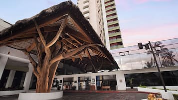 A modern building with a large tree sculpture in front, a glass facade, and a red brick pathway.