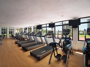 A gym with treadmills and ellipticals, large windows, and a view of greenery and buildings. - El Cid El Moro Beach Hotel - All Inclusive (Mazatlán)