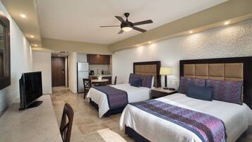 A hotel room with two beds, a kitchenette, a ceiling fan, and a TV.