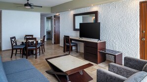 A modern living room with a flat-screen TV, a dining area with wooden chairs, and a sofa. - El Cid El Moro Beach Hotel - All Inclusive (Mazatlán)