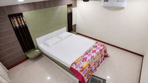 A single bed with a white mattress and pillows, a colorful blanket, a green headboard, and a small bedside table. - Park Inn (Port Blair)
