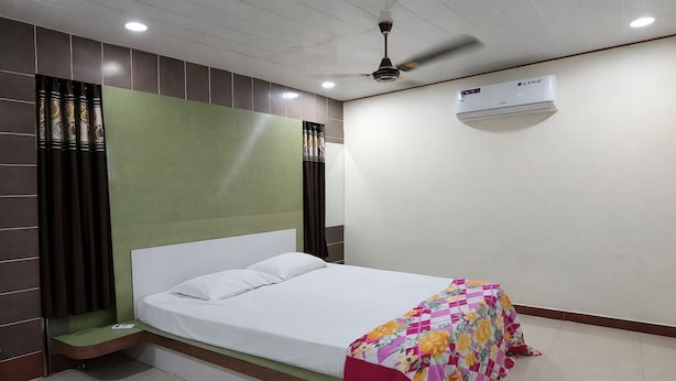 A hotel room with a bed, a green headboard, a ceiling fan, an air conditioning unit, and a window with curtains. - Park Inn (Port Blair)