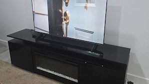 A flat-screen TV on a black entertainment center with a shelf below. - Cy Becker Drive 2023 Luxury Home (Edmonton)